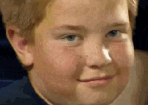 Close-up portrait of a young boy with reddish-blonde hair smiling slightly at the camera against a dark background